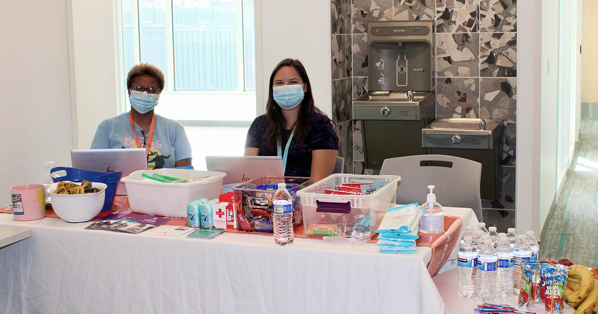 Two people sit at a table with hygiene supplies, food, and resources at the Community Health Fair.