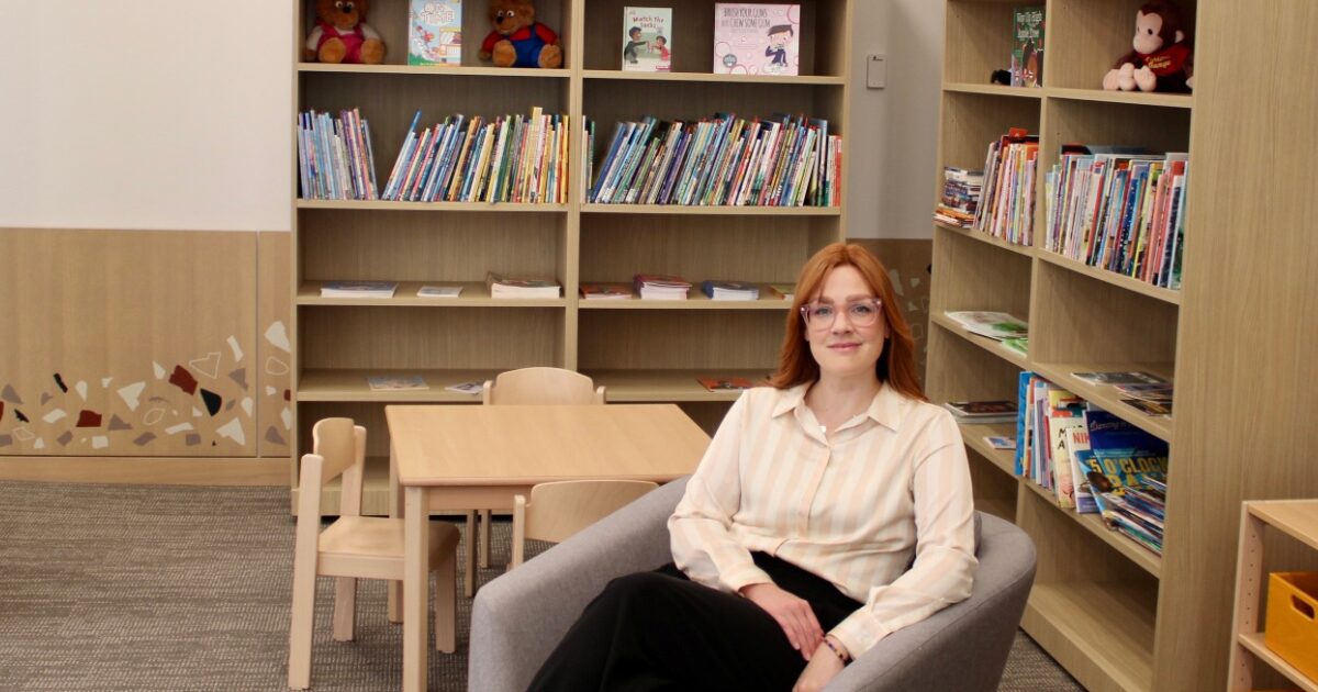 Woman sits in a chair with bookshelves behind her
