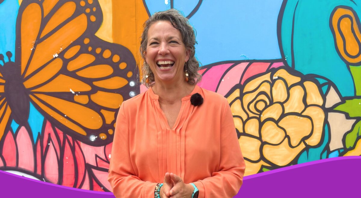 New CEO of The Family Partnership Emily Larson smiling in front of a vibrant mural in South Minneapolis featuring a butterfly and large flowers, symbolizing growth and transformation.